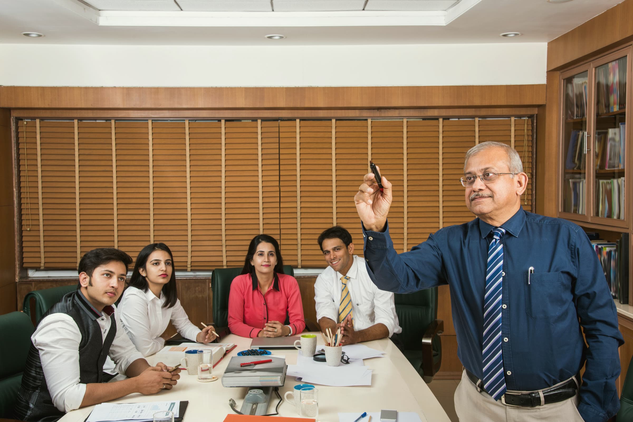 A senior leader presenting a plan to his team in a wood-panelled meeting room