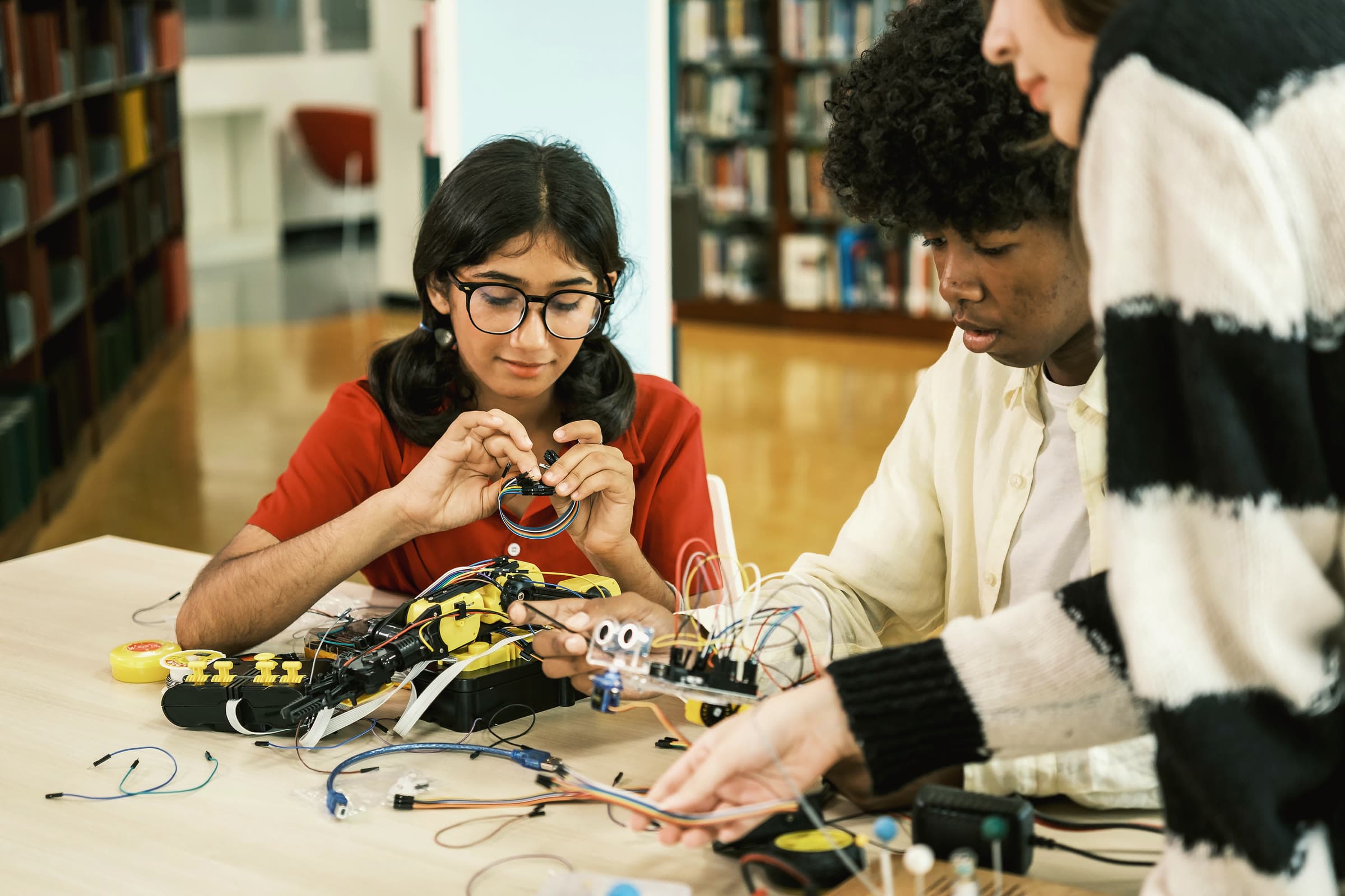 A student wiring a robotics kit with classmates in a school library