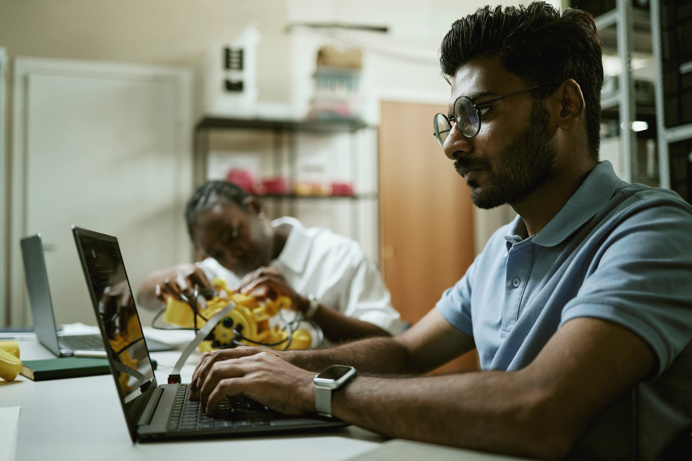 A participant coding on a laptop while another assembles a robot arm at a robotics workshop